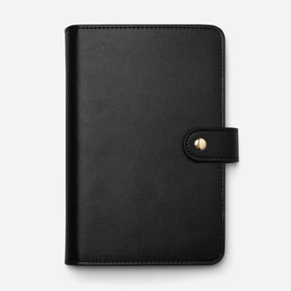 A black faux-leather planner cover with a snap-button strap closure, shown flat against a light gray background.