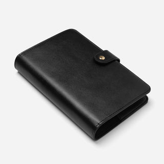 A black leather planner binder with a snap-button closure, shown at an angle on a light gray background.